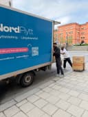 Nordflytts blå flyttbil med tjänstetext och flyttare på en gata i Stockholm.