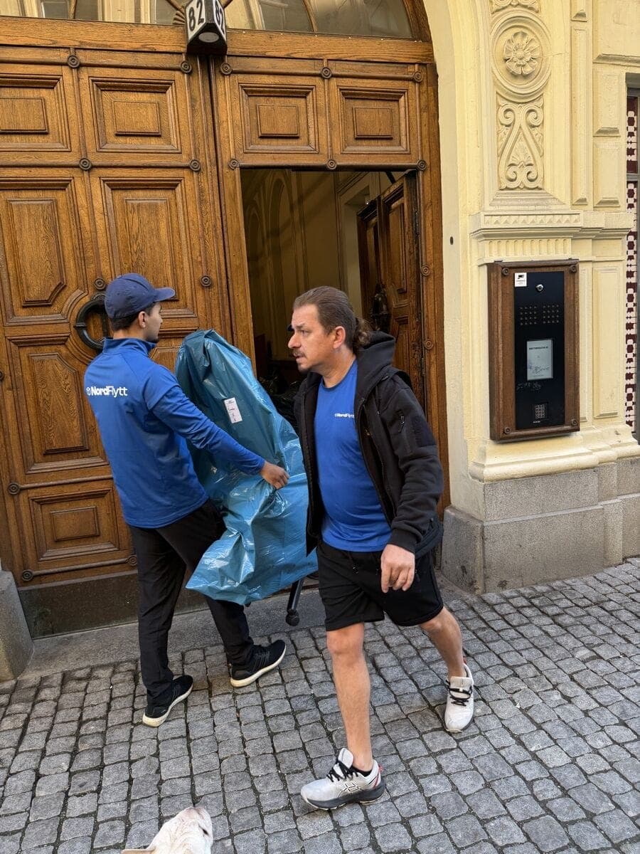 Två flyttare i Nordflytts kläder bär en blåemballerad möbel genom en port under Strongers flyttdag