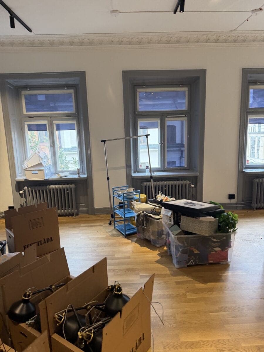 Packade flyttlådor och kvarvarande inventarier i en ljus kontorslokal med höga fönster